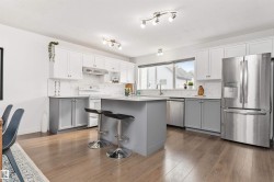 Modern kitchen featuring two-tone cabinetry, stainless steel appliances, a center island with quartz countertop seating, Vinyl plank flooring, and track lighting - 