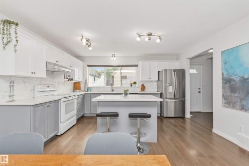 Kitchen featuring two-tone cabinetry, stainless steel refrigerator, white appliances, a quartz island with seating, and Vinyl plank flooring - 4121 Tompkins Way Nw, Edmonton, AB - Indoor Photo Showing Kitchen