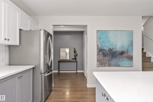 Stainless steel refrigerator, white shaker upper cabinetry, gray lower cabinetry, light-toned quartz countertops, and Vinyl plank flooring - 4121 Tompkins Way Nw, Edmonton, AB - Indoor Photo Showing Kitchen