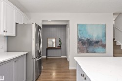 Stainless steel refrigerator, white shaker upper cabinetry, gray lower cabinetry, light-toned quartz countertops, and Vinyl plank flooring - 