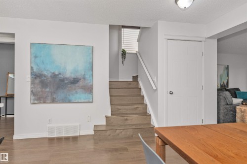 Wood-finish flooring throughout, white trim, and a staircase with a white railing - 4121 Tompkins Way Nw, Edmonton, AB - Indoor Photo Showing Other Room
