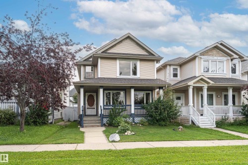 Two-story property featuring light-colored siding, a covered front porch with white columns, and a dark-colored front door with an oval glass insert - 4121 Tompkins Way Nw, Edmonton, AB - Outdoor With Deck Patio Veranda With Facade