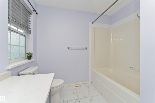 White tiled flooring, white bathtub with integrated shower, white toilet, and a white quartz countertop - 4121 Tompkins Way Nw, Edmonton, AB - Indoor Photo Showing Bathroom
