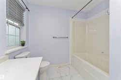 White tiled flooring, white bathtub with integrated shower, white toilet, and a white quartz countertop - 
