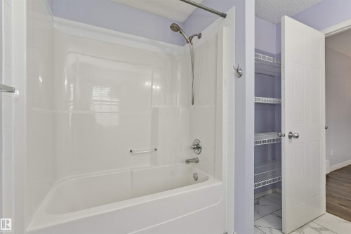 White bathtub with an integrated shower, chrome fixtures, and adjacent built-in shelving - 4121 Tompkins Way Nw, Edmonton, AB - Indoor Photo Showing Bathroom