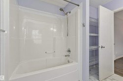White bathtub with an integrated shower, chrome fixtures, and adjacent built-in shelving - 