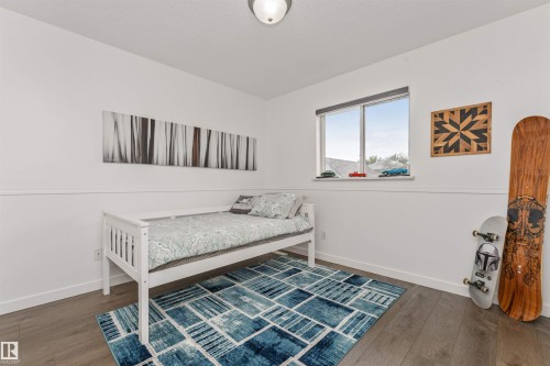 White walls with wainscoting, wood-finish flooring, and a single window with a roller shade - 4121 Tompkins Way Nw, Edmonton, AB - Indoor Photo Showing Bedroom