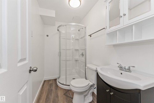 Wood-finish flooring, white walls, enclosed corner shower, dark wood-finish vanity, and wall-mounted storage cabinet - 4121 Tompkins Way Nw, Edmonton, AB - Indoor Photo Showing Bathroom