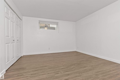 Wood-finish flooring, white walls, bi-fold closet doors, and an egress window - 4121 Tompkins Way Nw, Edmonton, AB - Indoor Photo Showing Other Room