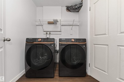 Laundry area with modern dark-finish washer and dryer appliances, wood-finish flooring, and a wall-mounted wire shelving unit - 4121 Tompkins Way Nw, Edmonton, AB - Indoor Photo Showing Laundry Room