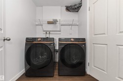 Laundry area with modern dark-finish washer and dryer appliances, wood-finish flooring, and a wall-mounted wire shelving unit - 