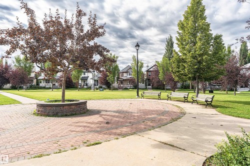 Expansive green space featuring mature trees, a paved brick pathway, and a central tree planter - 4121 Tompkins Way Nw, Edmonton, AB - Outdoor
