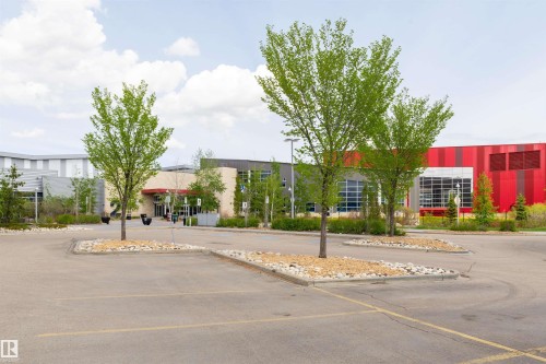 Paved parking area with landscaped tree islands, modern building architecture, and a prominent red facade - 4121 Tompkins Way Nw, Edmonton, AB - Outdoor