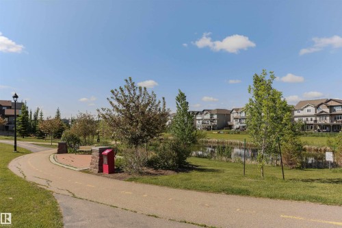 Established neighborhood featuring a paved walking path, mature trees, a tranquil pond, and residential structures with multiple balconies - 4121 Tompkins Way Nw, Edmonton, AB - Outdoor