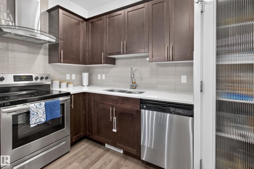 Contemporary kitchen featuring dark wood cabinetry, stainless steel appliances, light solid-surface countertops, and a subway tile backsplash - 17305 73 Street Nw, Edmonton, AB - Indoor Photo Showing Kitchen With Stainless Steel Kitchen With Double Sink With Upgraded Kitchen