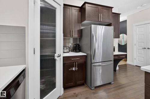 Kitchen featuring dark wood cabinetry, stainless steel refrigerator, white countertops, and wood-finish flooring - 17305 73 Street Nw, Edmonton, AB - Indoor Photo Showing Kitchen With Stainless Steel Kitchen