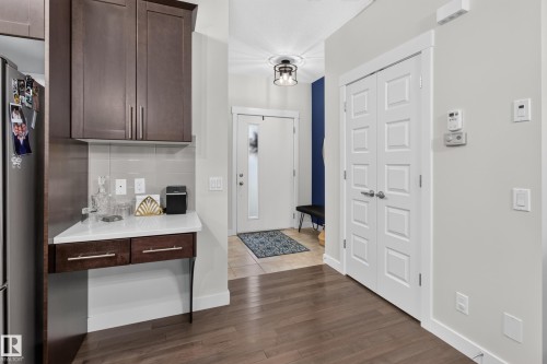 Entry area featuring wood-finish flooring, a built-in counter with white stone-finish surface, dark wood cabinetry, white paneled doors, and an overhead drum light fixture - 17305 73 Street Nw, Edmonton, AB - Indoor