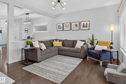 Living area featuring wood-finish flooring, a contemporary semi-flush mount light fixture, and a partial wall dividing spaces - 17305 73 Street Nw, Edmonton, AB - Indoor Photo Showing Living Room
