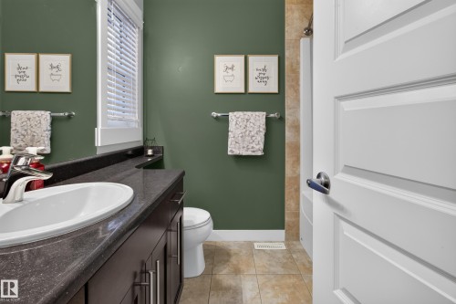 Bathroom featuring a dark wood-finish vanity with a white oval sink, dark speckled countertop, and brushed nickel hardware - 17305 73 Street Nw, Edmonton, AB - Indoor Photo Showing Bathroom