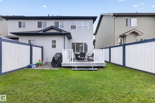 Rear exterior featuring light gray siding, a private backyard with a manicured lawn, a raised wood-finish deck, and a sliding glass door - 17305 73 Street Nw, Edmonton, AB - Outdoor With Deck Patio Veranda With Exterior