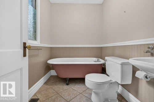 Freestanding clawfoot tub, beadboard wainscoting, tiled flooring, pedestal sink, and a privacy window - 9026 92 Street Nw, Edmonton, AB - Indoor Photo Showing Bathroom