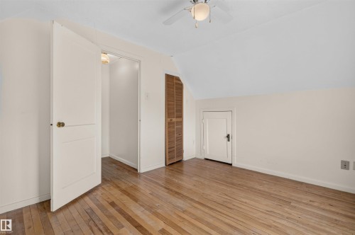 Wood-finish flooring, white walls, angled ceiling, ceiling fan with integrated lighting, and louvered closet doors - 9026 92 Street Nw, Edmonton, AB - Indoor Photo Showing Other Room