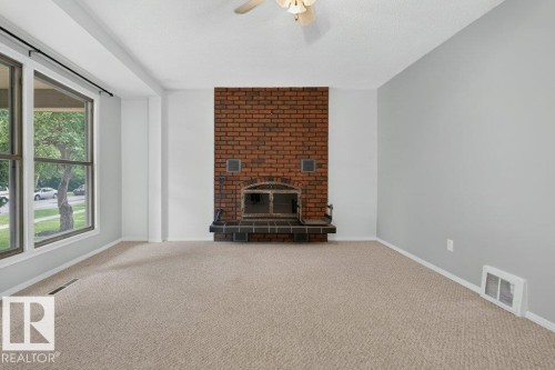Brick fireplace with a metal grate, neutral carpeting, and a ceiling fan - 9026 92 Street Nw, Edmonton, AB - Indoor With Fireplace
