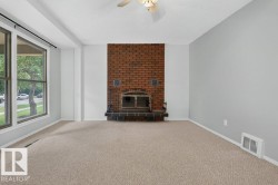 Brick fireplace with a metal grate, neutral carpeting, and a ceiling fan - 