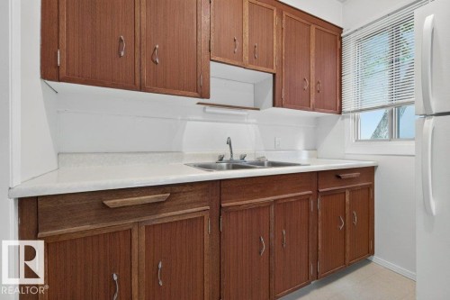 Wood-finish cabinetry with silver-tone hardware, white countertops, and a double basin sink - 9026 92 Street Nw, Edmonton, AB - Indoor Photo Showing Kitchen With Double Sink