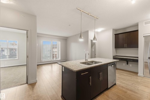 Kitchen island with an undermount dual-basin sink, stainless steel dishwasher, and pendant lighting - #414 5510 Schonsee Dr Nw, Edmonton, AB - Indoor Photo Showing Kitchen With Double Sink
