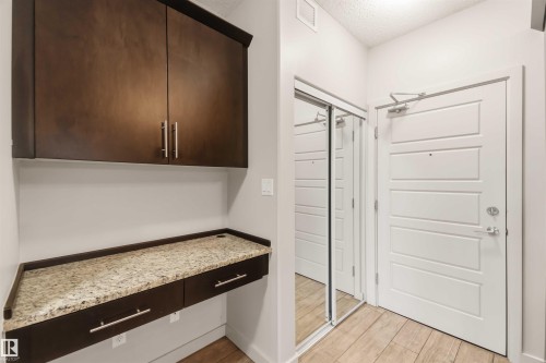 Built-in desk with a stone-finish countertop, dark wood-finish cabinetry, and a mirrored closet - #414 5510 Schonsee Dr Nw, Edmonton, AB - Indoor Photo Showing Other Room