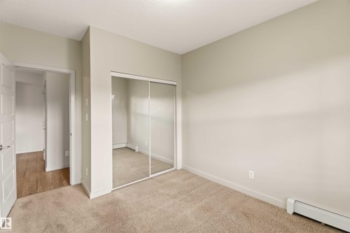 Soft neutral wall paint with carpet flooring, mirrored closet doors, and white paneled doors - #414 5510 Schonsee Dr Nw, Edmonton, AB - Indoor Photo Showing Other Room