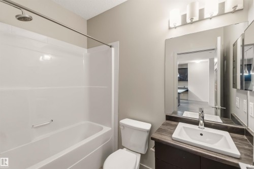 Bathroom featuring a combination shower and tub, a vanity with an integrated sink, a large mirror, and a wall-mounted light fixture - #414 5510 Schonsee Dr Nw, Edmonton, AB - Indoor Photo Showing Bathroom