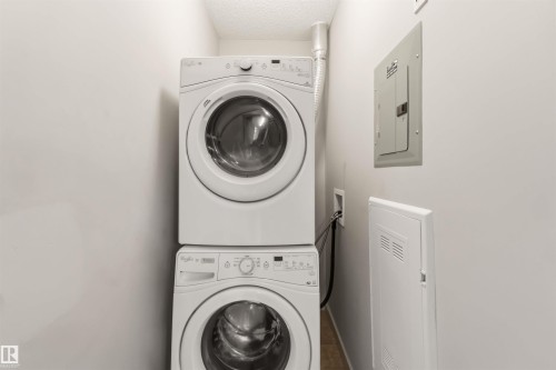 Stacked laundry appliances with front-load design, recessed utility panel, and wood-finish flooring - #414 5510 Schonsee Dr Nw, Edmonton, AB - Indoor Photo Showing Laundry Room
