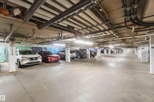 Underground parking garage featuring concrete flooring, exposed ceiling utilities, and fluorescent lighting fixtures - #414 5510 Schonsee Dr Nw, Edmonton, AB - Indoor Photo Showing Garage