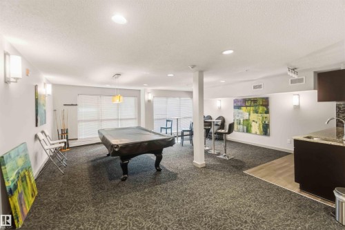 Spacious recreation room featuring recessed lighting, wall sconces, wood-finish flooring, and a built-in wet bar with a stone countertop - #414 5510 Schonsee Dr Nw, Edmonton, AB - Indoor Photo Showing Other Room