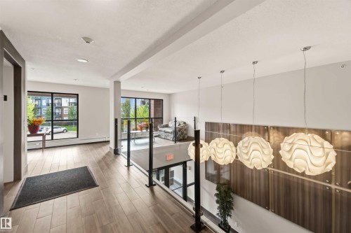 Open concept common area featuring large windows, wood-finish flooring, glass panel railings, and modern pendant lighting - #414 5510 Schonsee Dr Nw, Edmonton, AB - Indoor Photo Showing Other Room