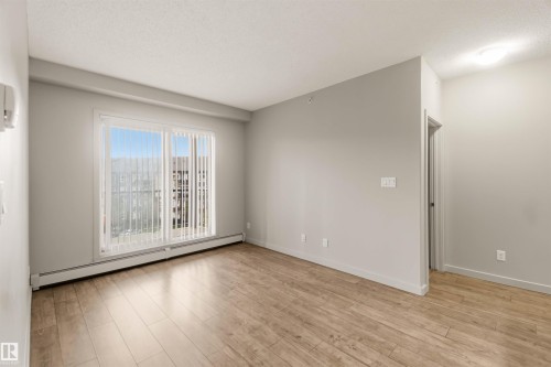 Wood-finish flooring, light grey wall paint, large sliding glass door, white vertical blinds, and a flush mount ceiling light - #414 5510 Schonsee Dr Nw, Edmonton, AB - Indoor Photo Showing Other Room