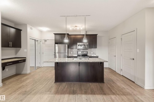 Kitchen featuring a central island with a sink, stainless steel appliances, dark wood-finish cabinetry, and light wood-finish flooring - #414 5510 Schonsee Dr Nw, Edmonton, AB - Indoor Photo Showing Kitchen With Stainless Steel Kitchen With Upgraded Kitchen