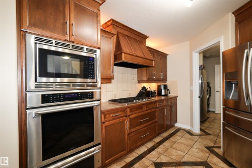 Kitchen featuring stainless steel appliances, wood cabinetry, built-in microwave and oven, and a gas cooktop with an integrated range hood - 9606 82 Avenue, Morinville, AB 