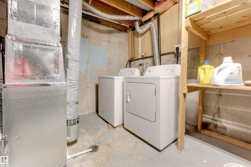 Dedicated laundry area featuring a washer and dryer, exposed concrete walls, concrete flooring, and overhead wooden shelving - #37 1411 Mill Woods Rd E Nw, Edmonton, AB - Indoor Photo Showing Laundry Room