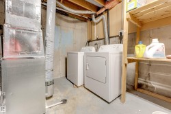 Dedicated laundry area featuring a washer and dryer, exposed concrete walls, concrete flooring, and overhead wooden shelving - 
