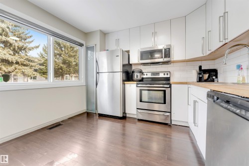Kitchen featuring stainless steel appliances, white cabinetry, wood-finish countertops, and wood-finish flooring - #37 1411 Mill Woods Rd E Nw, Edmonton, AB - Indoor Photo Showing Kitchen