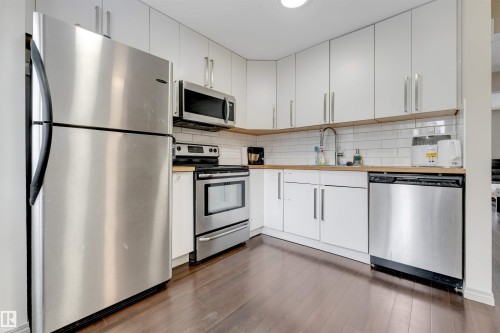 Kitchen featuring stainless steel appliances, white cabinetry, wood-finish countertops, subway tile backsplash, and wood-finish flooring - #37 1411 Mill Woods Rd E Nw, Edmonton, AB - Indoor Photo Showing Kitchen