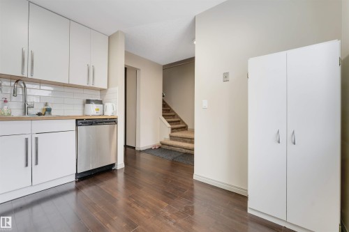White flat-panel cabinetry, stainless steel dishwasher, subway tile backsplash, wood-finish flooring, and built-in white storage cabinet - #37 1411 Mill Woods Rd E Nw, Edmonton, AB - Indoor Photo Showing Kitchen