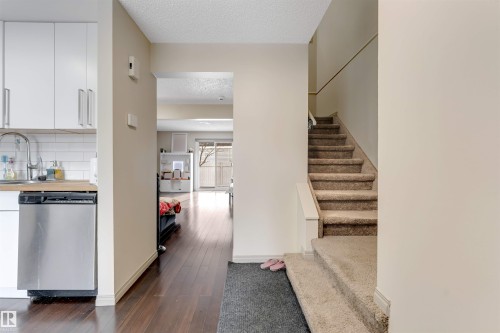Stainless steel dishwasher, white subway tile backsplash, wood-finish flooring, and carpeted staircase - #37 1411 Mill Woods Rd E Nw, Edmonton, AB - Indoor Photo Showing Other Room