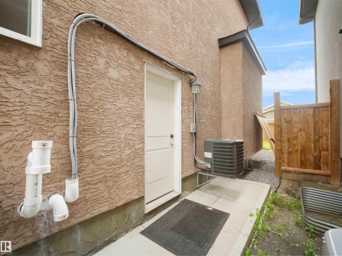 Stucco exterior with a white entry door, exterior lighting, a concrete pad, and a wooden privacy fence - 17020 62 Street Nw, Edmonton, AB - Outdoor With Exterior