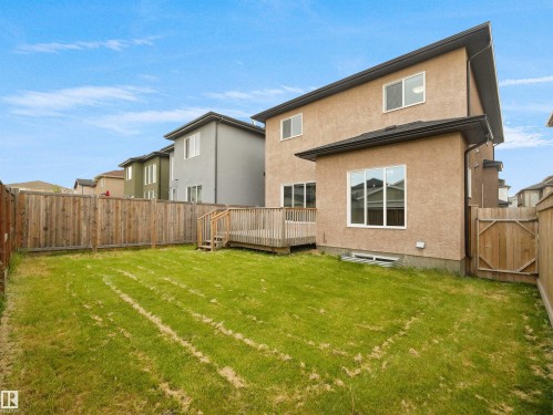 Expansive grassed yard with a wooden privacy fence, featuring a raised wood deck with railing and steps, and a stucco exterior - 17020 62 Street Nw, Edmonton, AB - Outdoor With Exterior