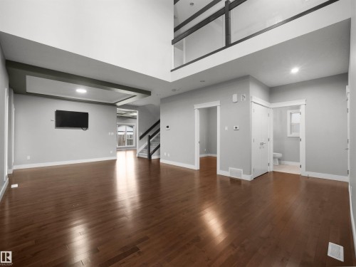 Expansive main living area featuring rich wood-finish flooring, a double-height ceiling, recessed lighting, an open staircase with glass railing, and a built-in ceiling detail - 17020 62 Street Nw, Edmonton, AB - Indoor