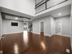 Expansive main living area featuring rich wood-finish flooring, a double-height ceiling, recessed lighting, an open staircase with glass railing, and a built-in ceiling detail - 